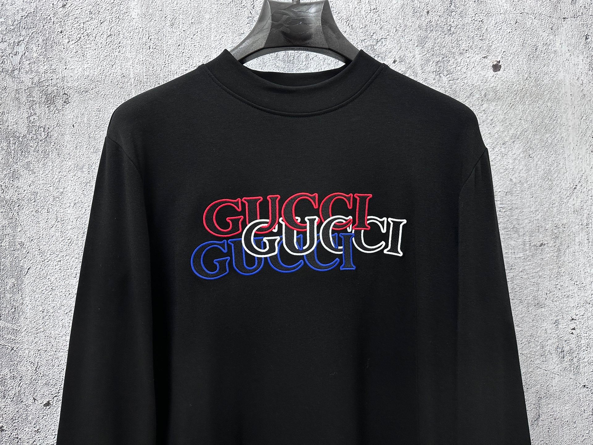 Black long-sleeve crewneck T-shirt with red and blue Gucci logo on chest
