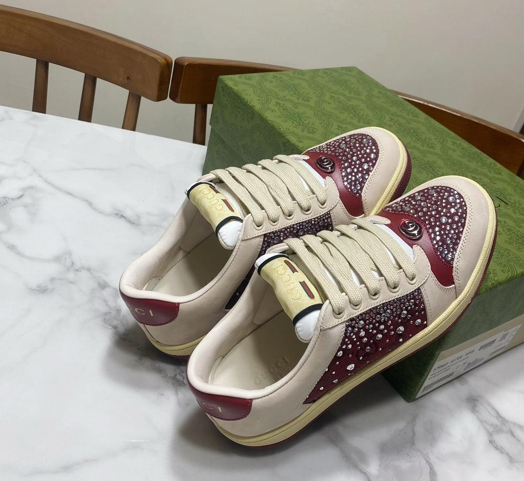 Unisex luxury sneakers by Gucci, front view showing cream laces and burgundy gem-style accents.
