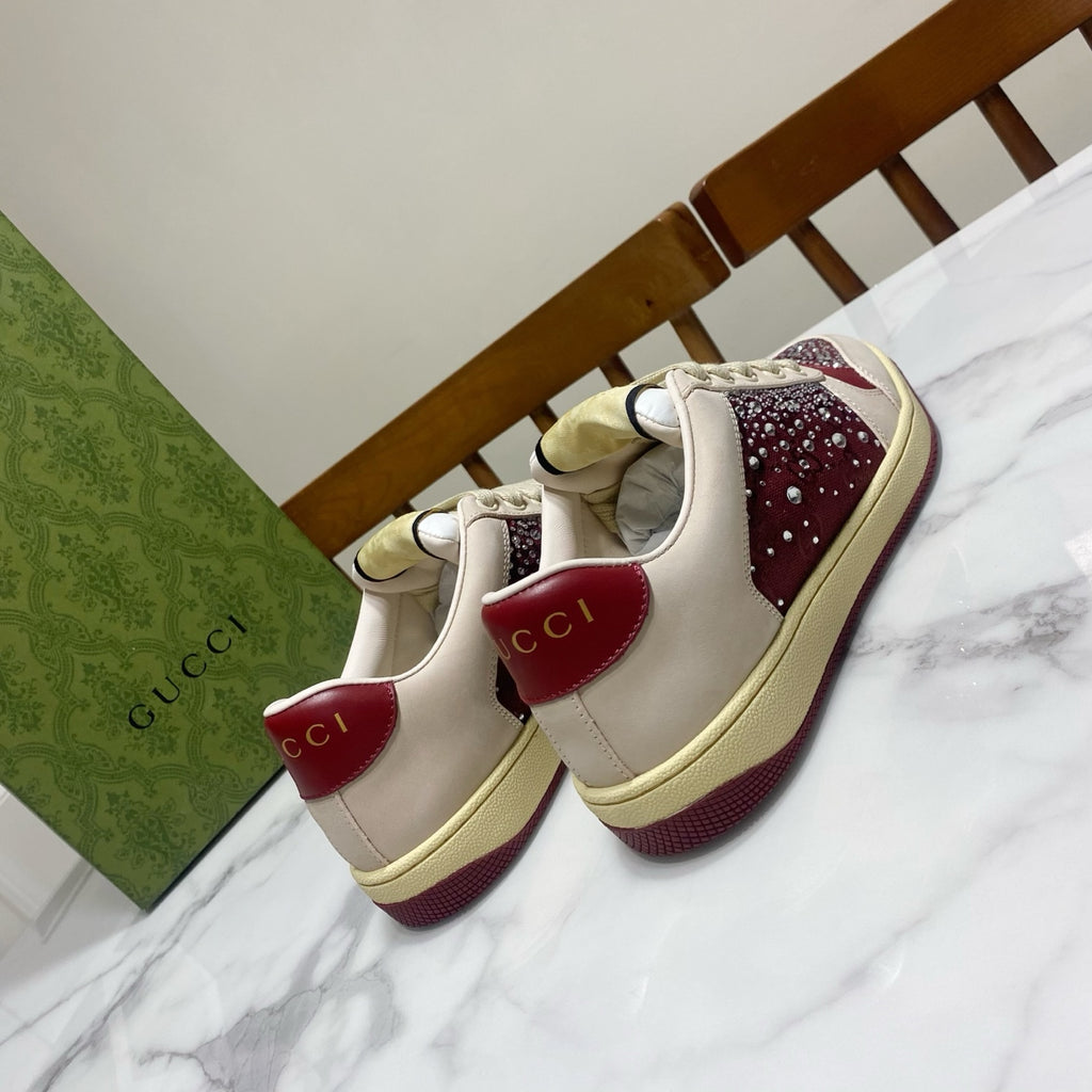 Unisex luxury sneakers by Gucci, cream uppers with burgundy heels and rhinestone detailing.