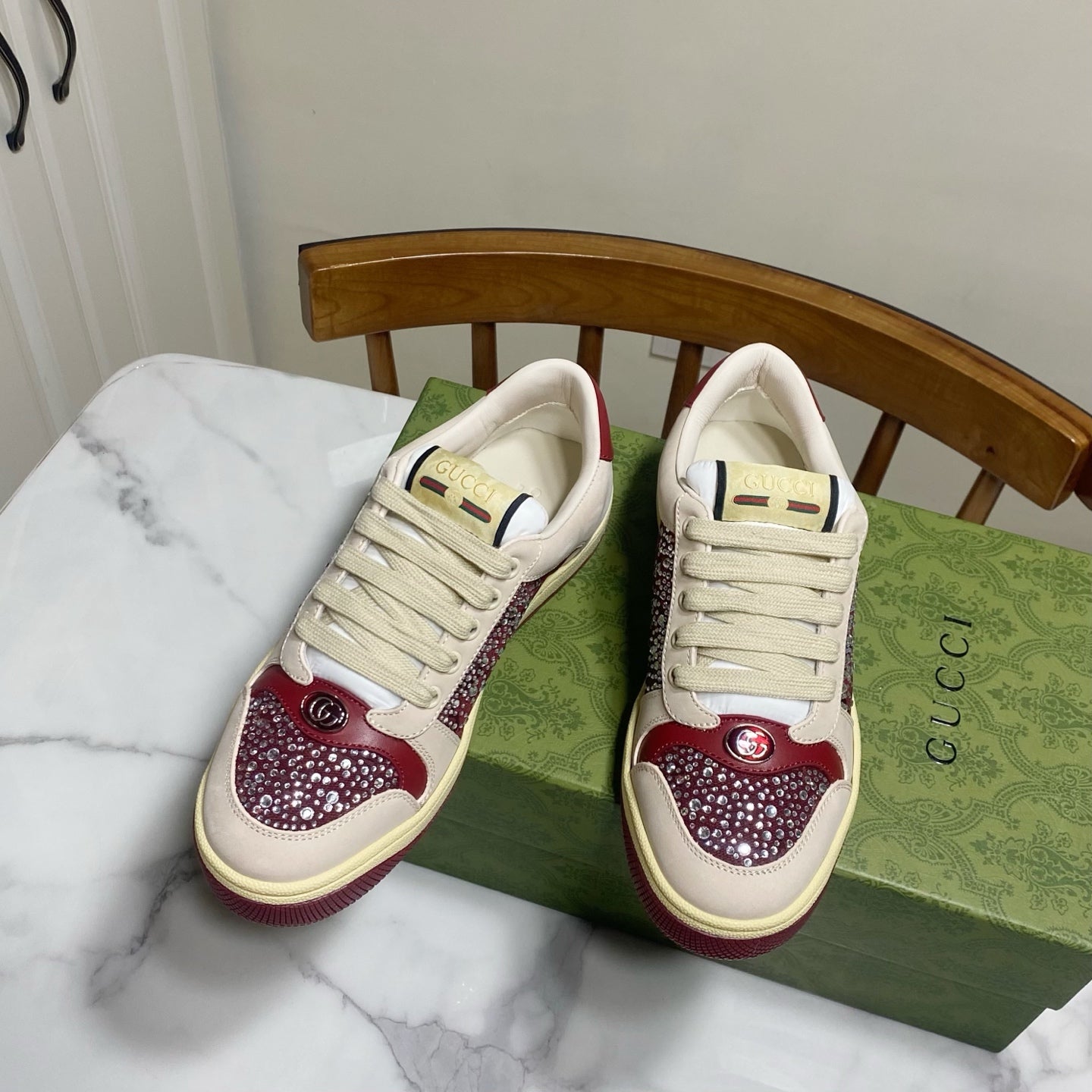 Unisex luxury sneakers by Gucci, pair of cream lace-up shoes with burgundy rhinestone accents.