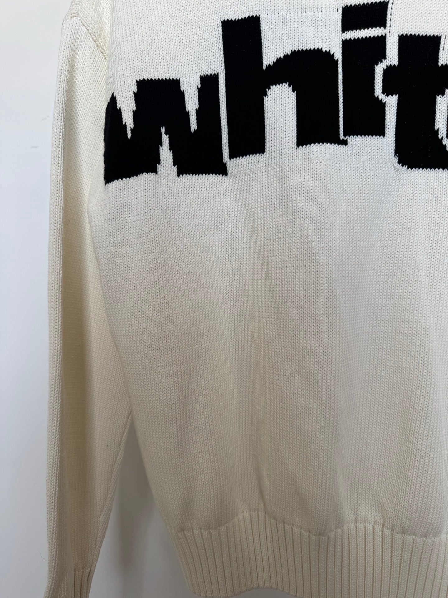 Off-white sweater back with large black logo lettering and ribbed hem