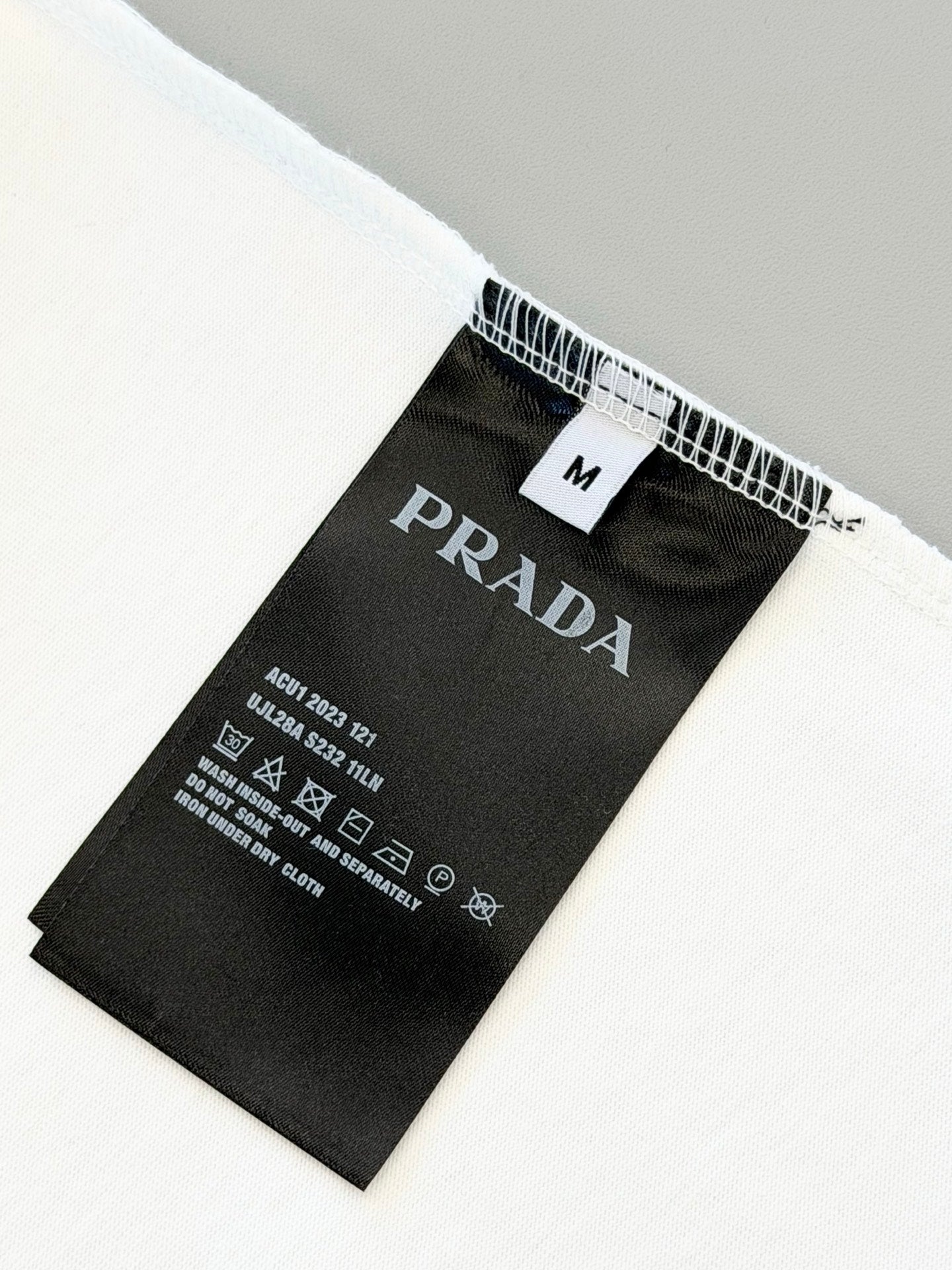 Black care label on white T-shirt with size M and PRADA branding
