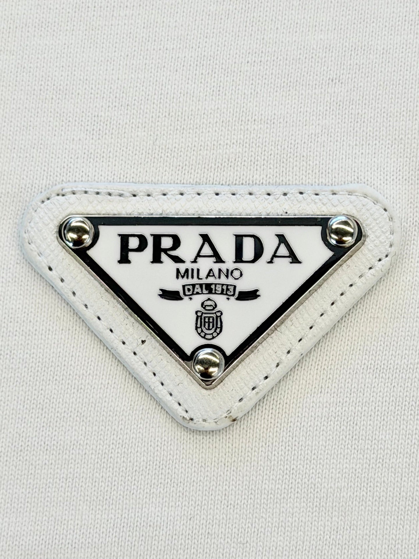 PRADA Milano triangular logo patch on white fabric