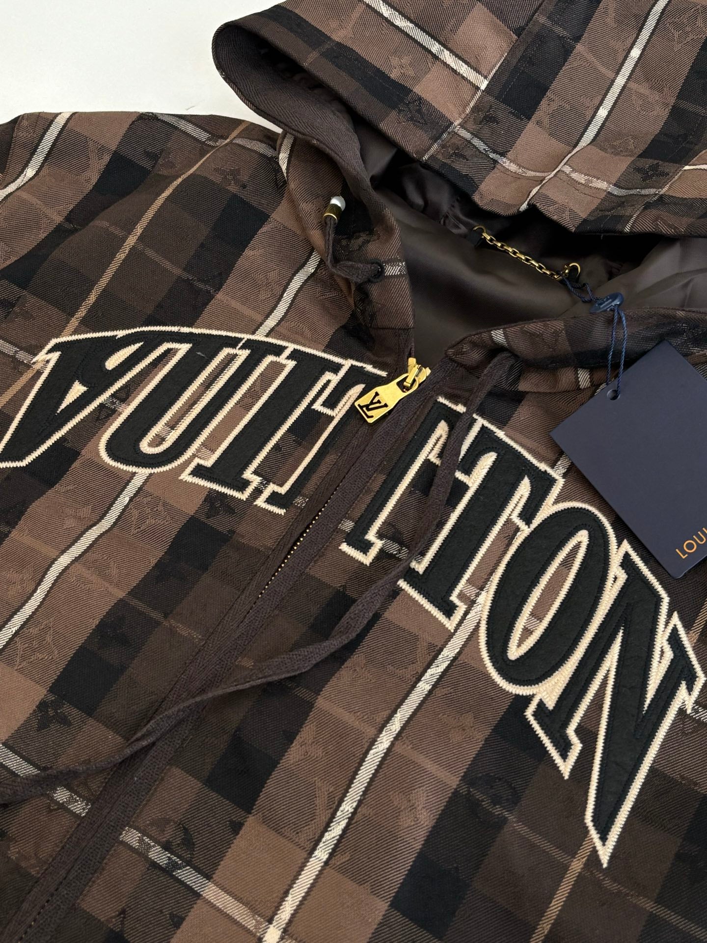Plaid jacket fabric detail with gold zipper pull and LV logo print