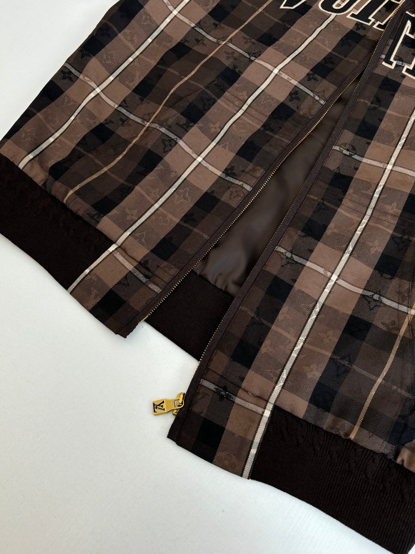 Plaid jacket front with black zipper and gold logo pull tab