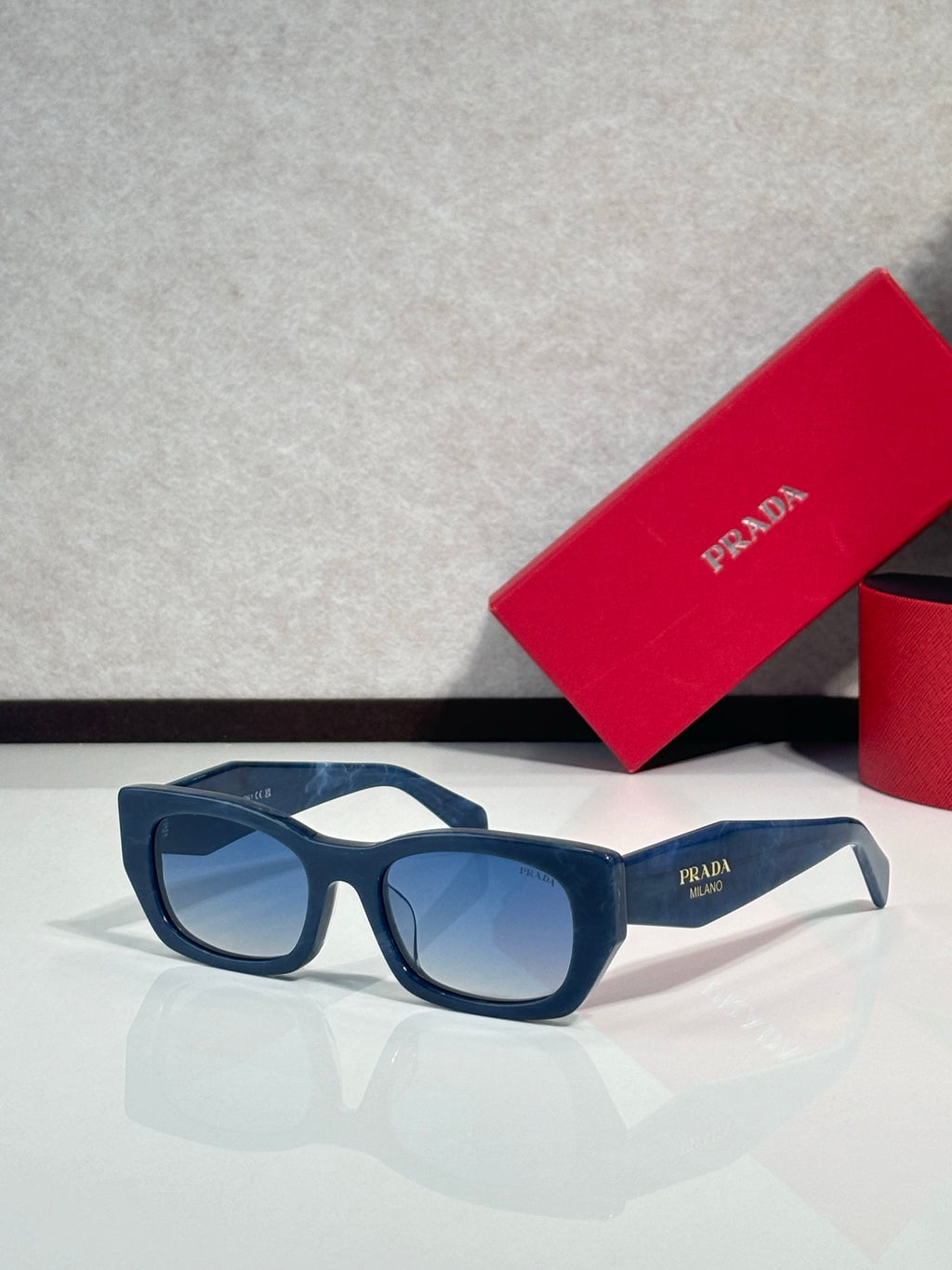 Sunglasses with dark blue frames and blue tinted lenses, Prada logo on temple.
