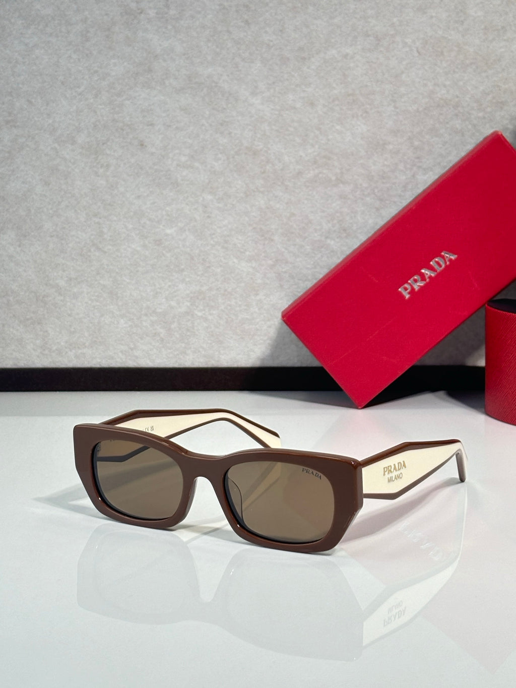 Sunglasses with tan frames and brown tinted lenses, Prada logo on temple.