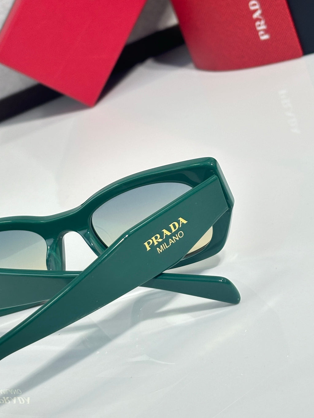 Green sunglasses temple with Prada Milano logo and angled hinge detail.