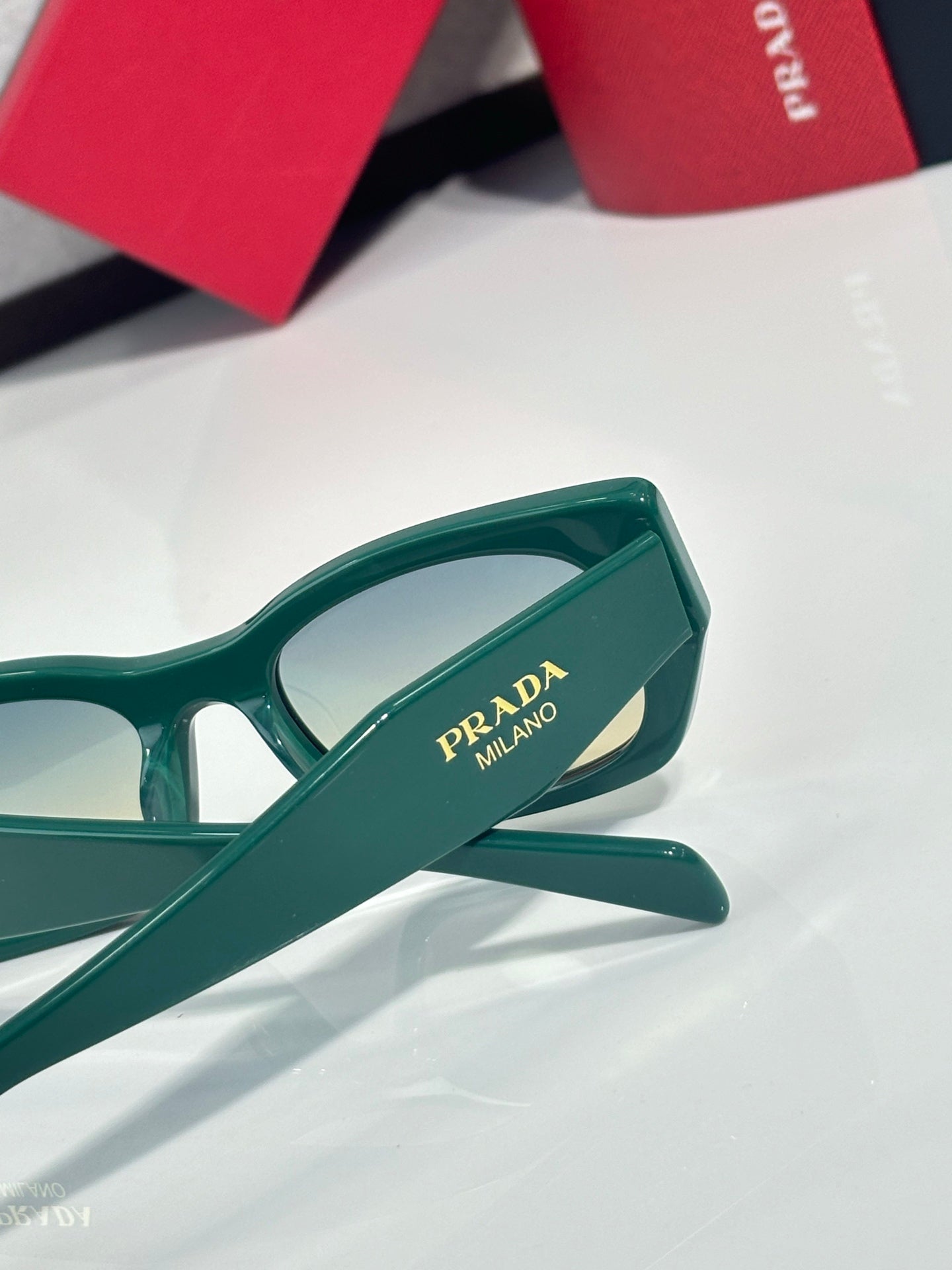 Green sunglasses temple with Prada Milano logo and angled hinge detail.