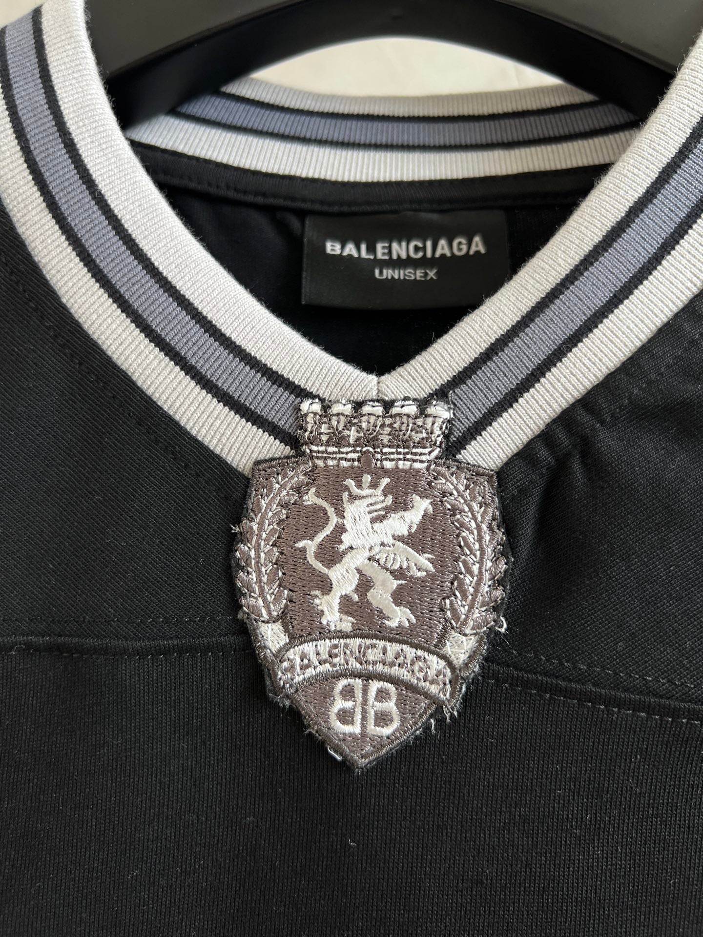 Black T-shirt neckline with striped trim and crest emblem; label reads BALENCIAGA UNISEX