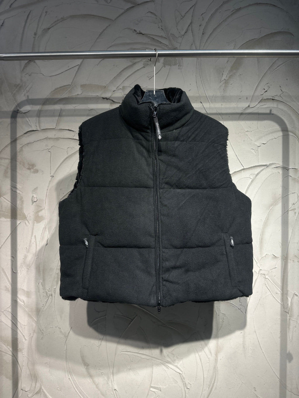 Black quilted puffer vest with front zipper and left sleeve pocket.