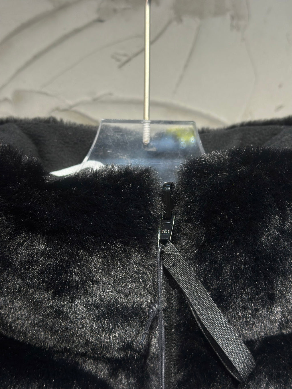 Black faux-fur puffer vest front detail with zipper tape and side strap.