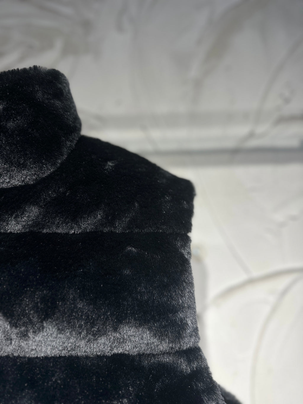 Black faux-fur puffer vest shoulder and upper chest texture view.