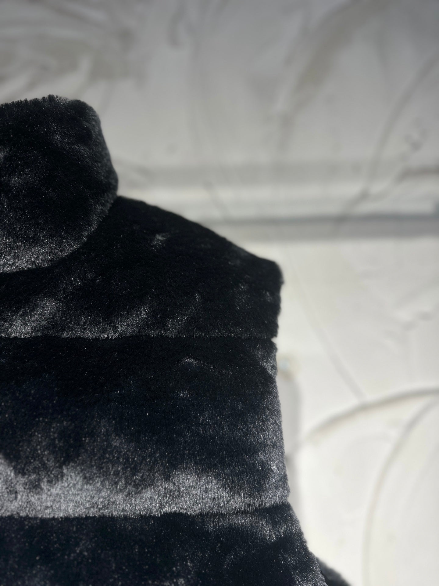 Black faux-fur puffer vest shoulder and upper chest texture view.