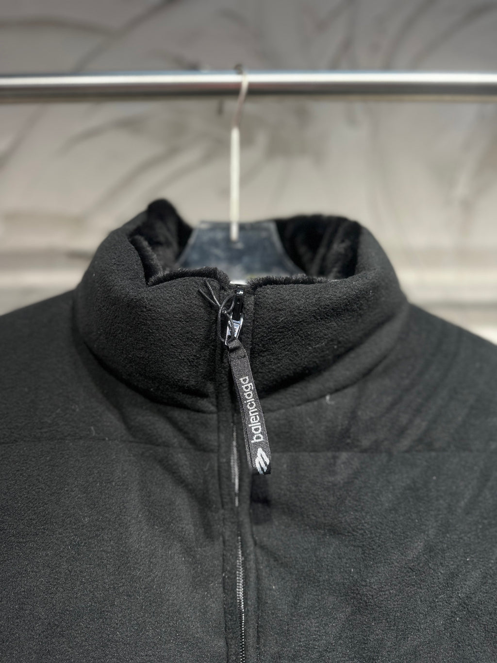 Black puffer vest hooded collar with zipper and vertical branding tag.