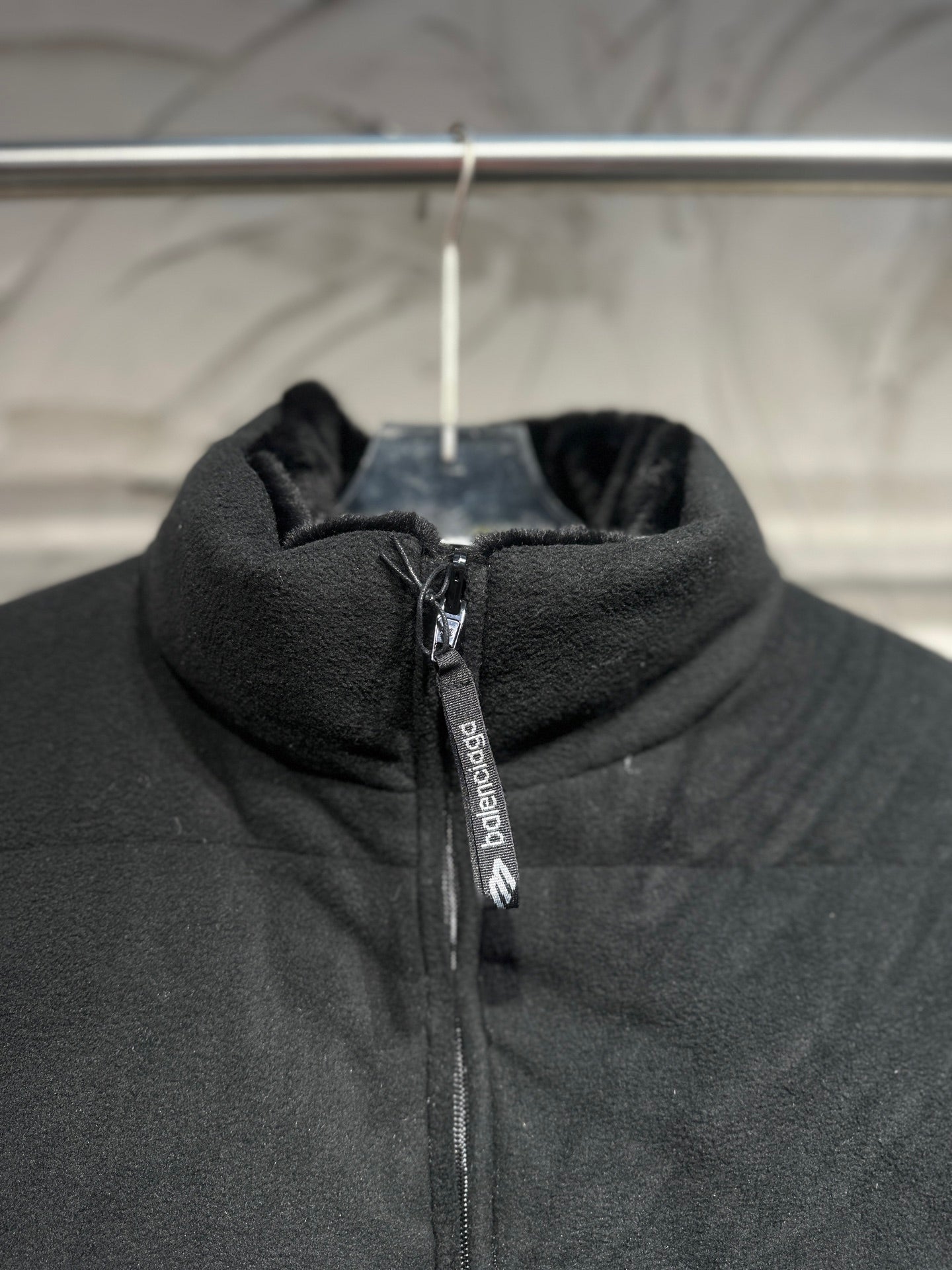 Black puffer vest hooded collar with zipper and vertical branding tag.