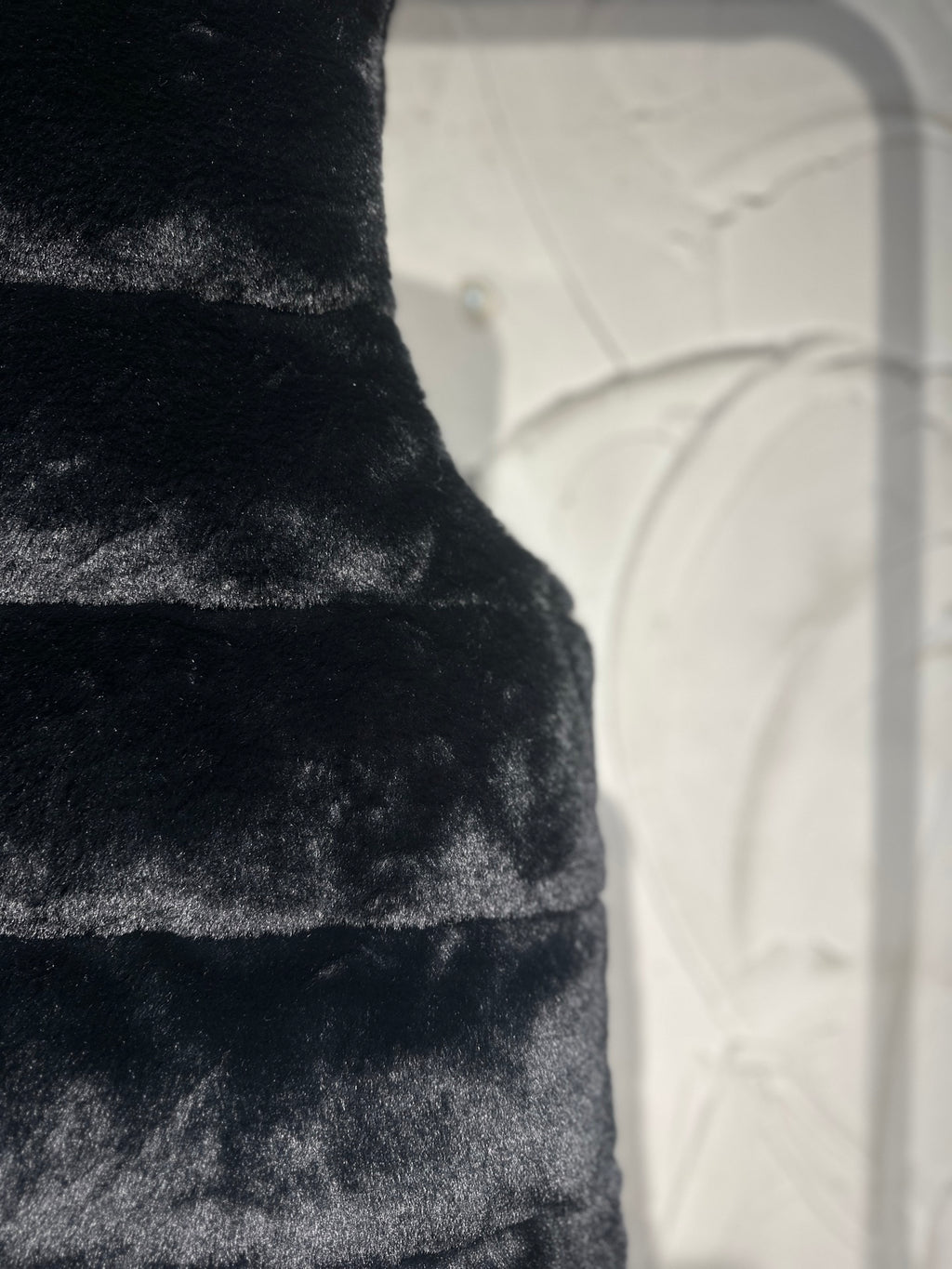 Black faux-fur puffer vest close-up of horizontal panel stitching.