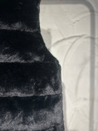 Black faux-fur puffer vest close-up of horizontal panel stitching.