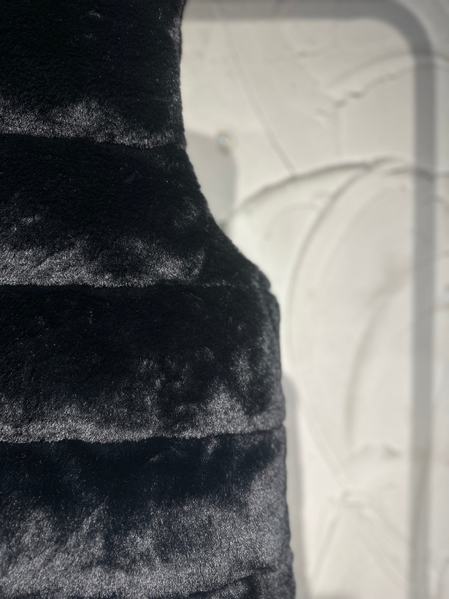 Black faux-fur puffer vest close-up of horizontal panel stitching.