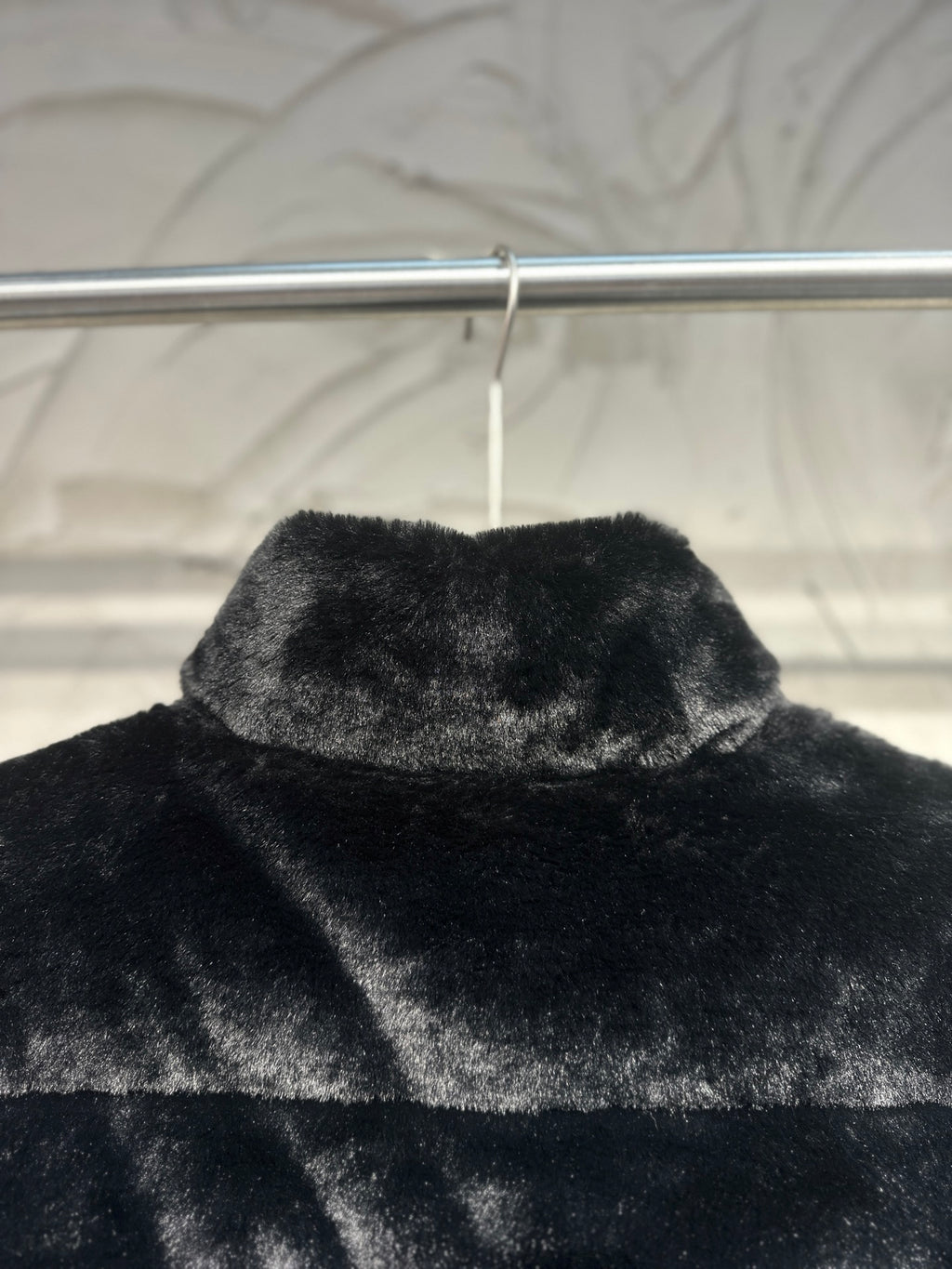 Black faux-fur puffer vest close-up of raised collar and top panel.