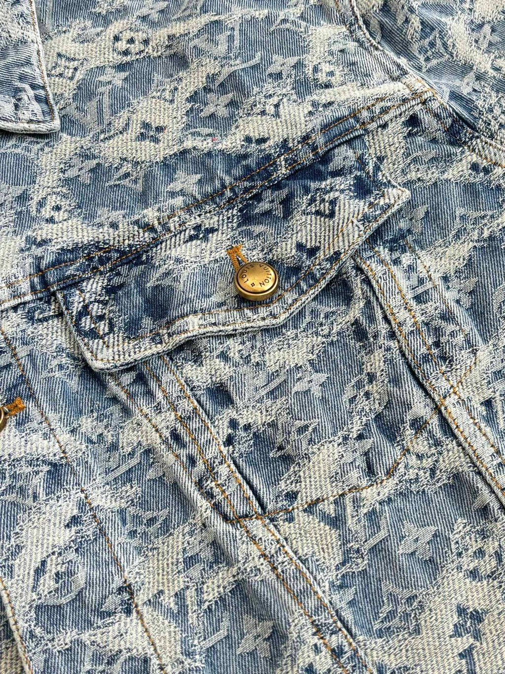Close-up of blue denim jacket pocket flap with gold button and stitched denim texture