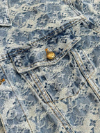 Close-up of blue denim jacket pocket flap with gold button and stitched denim texture