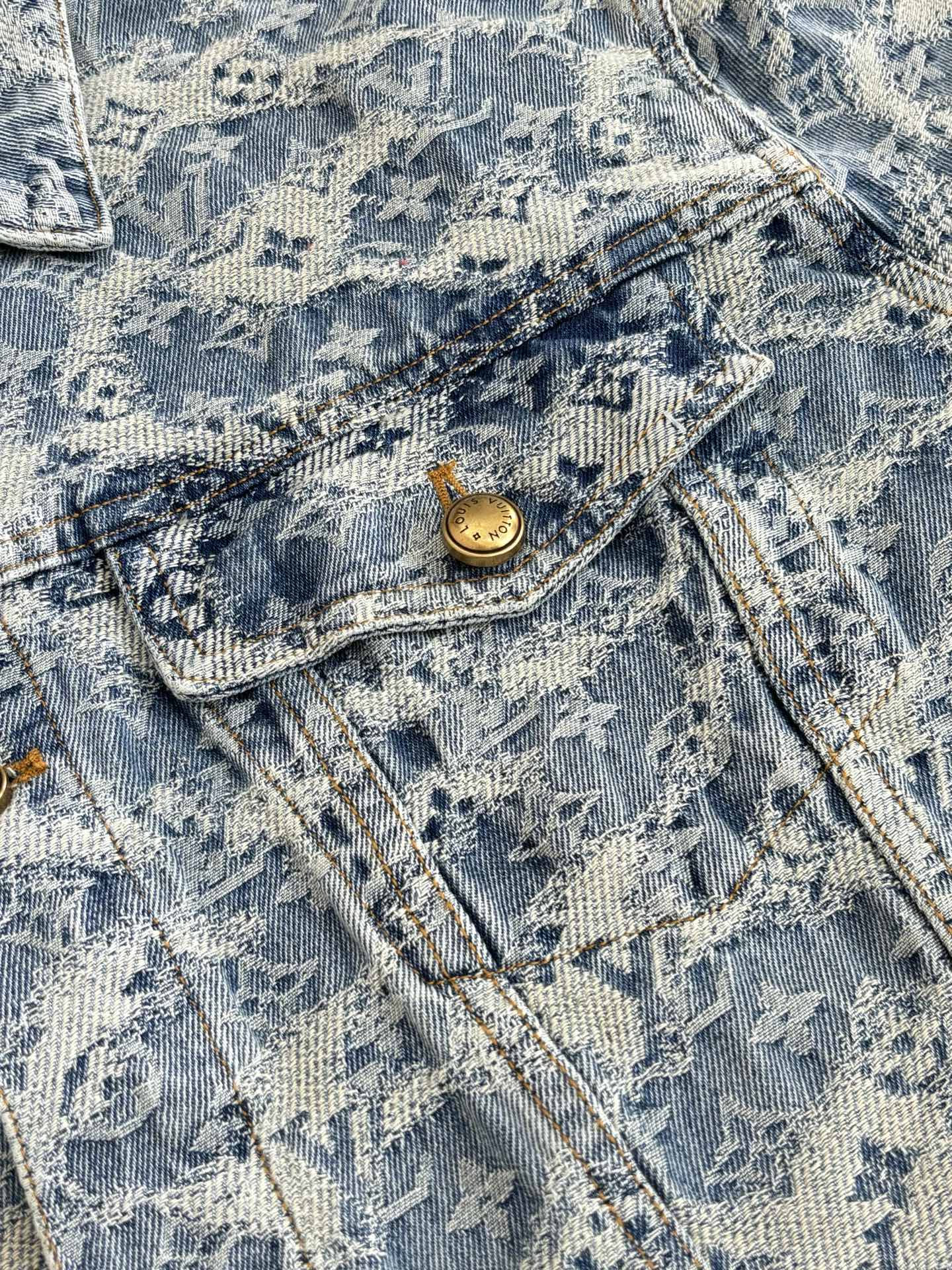 Close-up of blue denim jacket pocket flap with gold button and stitched denim texture