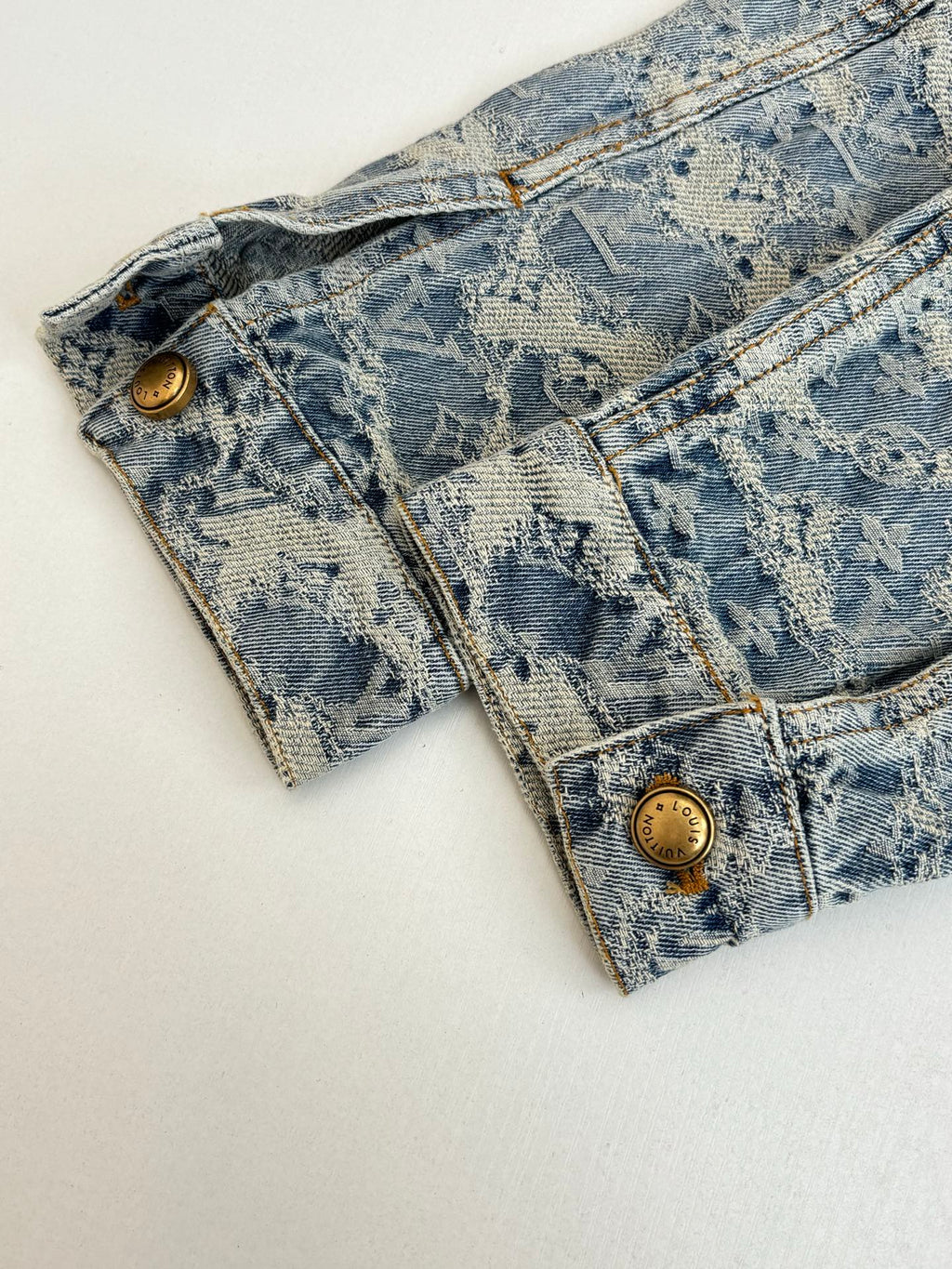 Long blue denim jacket with monogram pattern and gold snap buttons at cuffs