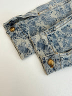Long blue denim jacket with monogram pattern and gold snap buttons at cuffs