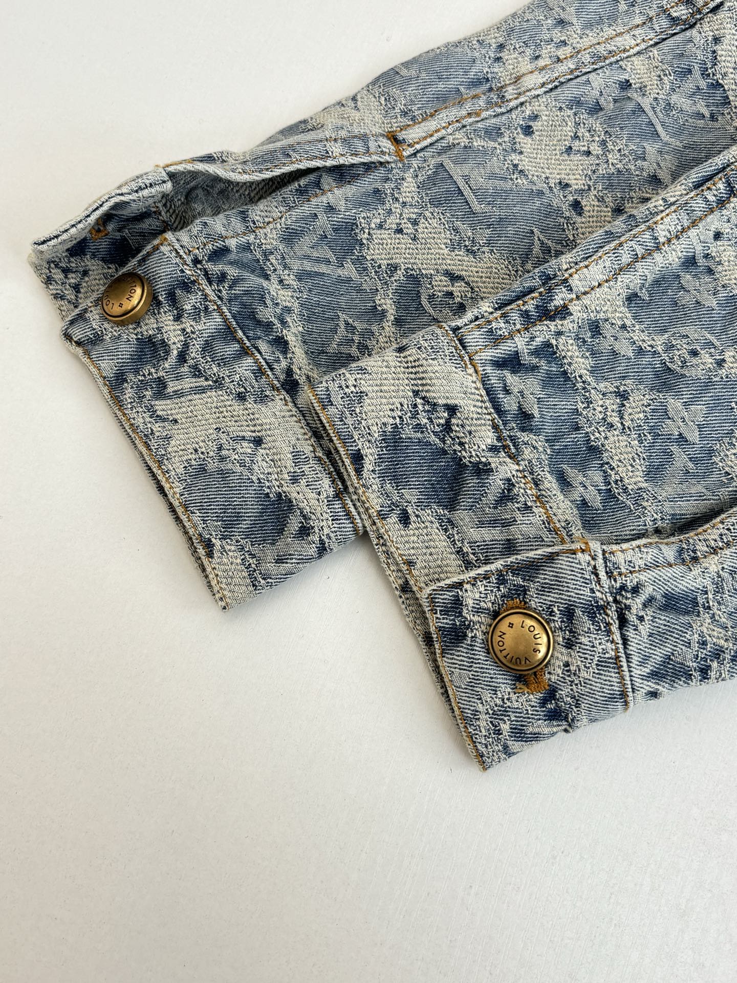 Long blue denim jacket with monogram pattern and gold snap buttons at cuffs
