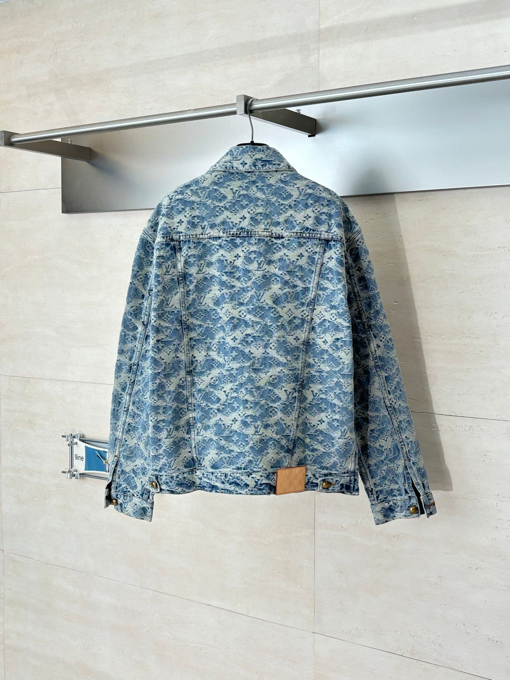 Back view of blue denim jacket with allover monogram pattern and button closure