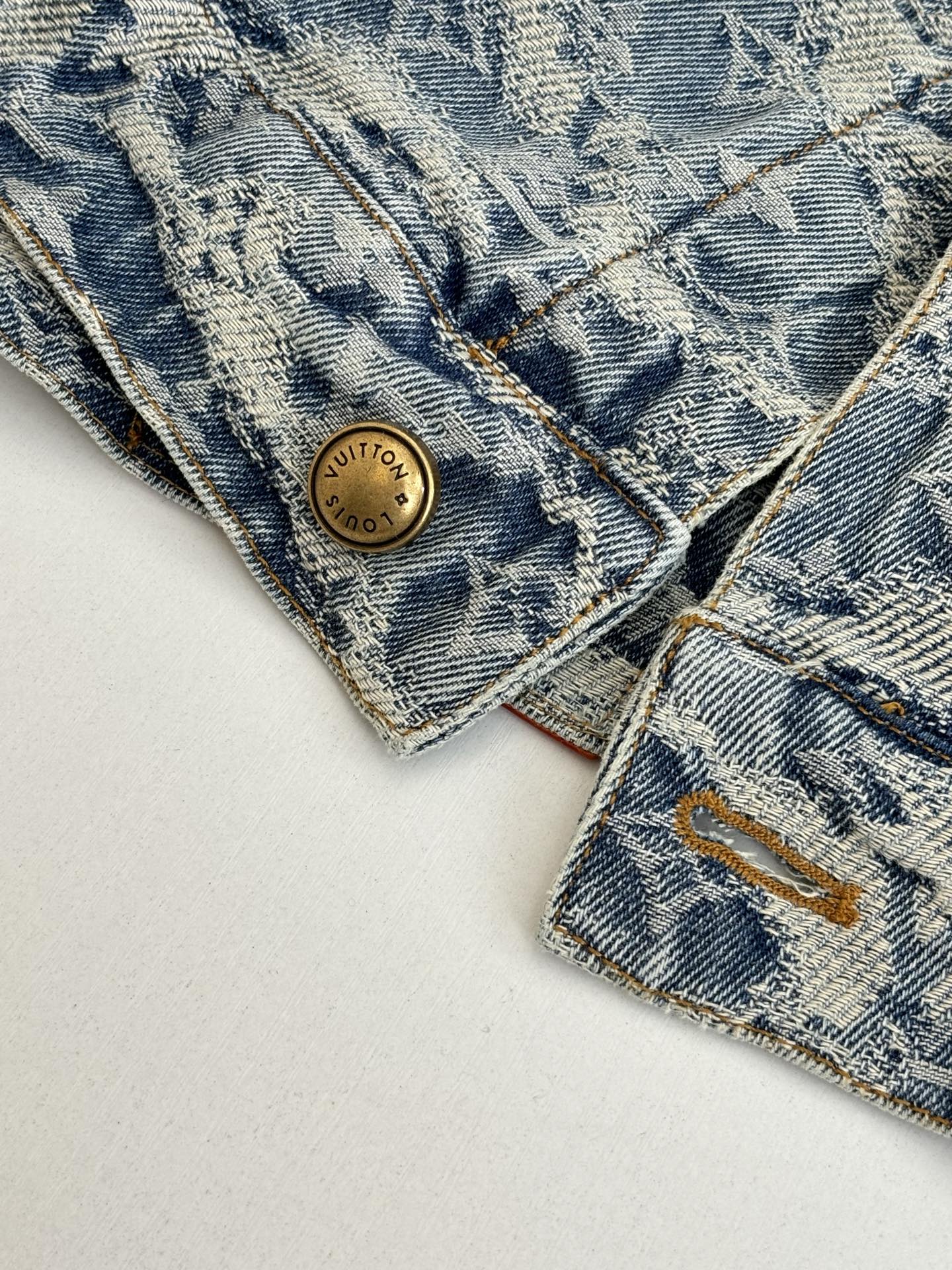 Close-up of blue denim monogram collar area with gold button and contrast stitching
