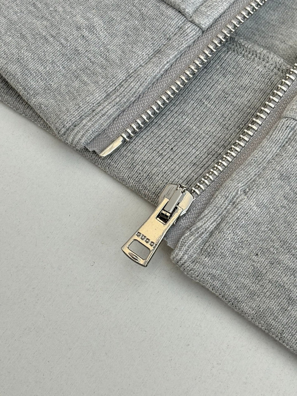 Grey zip jacket close-up with metal zipper pull and Gucci label