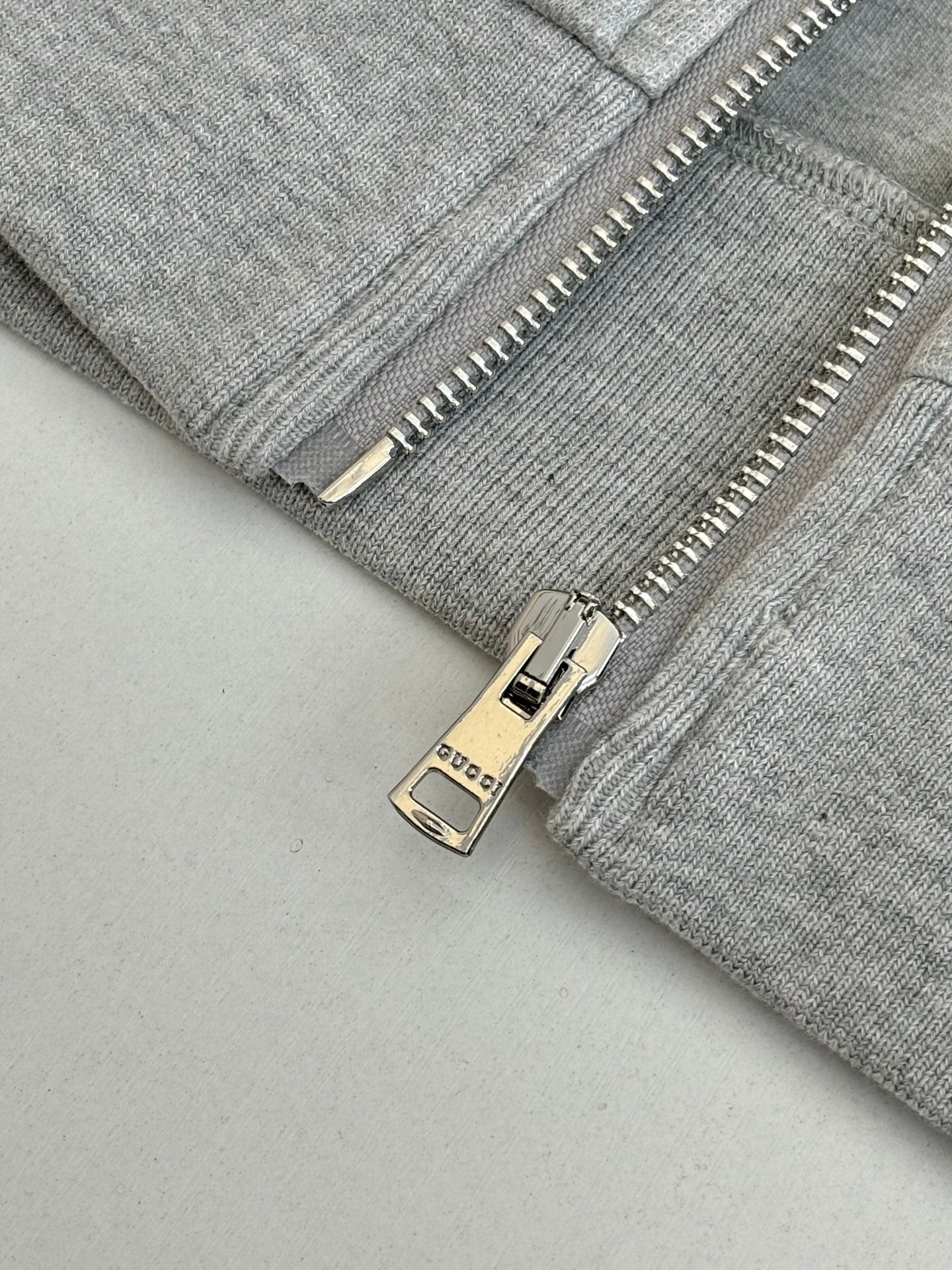 Grey zip jacket close-up with metal zipper pull and Gucci label