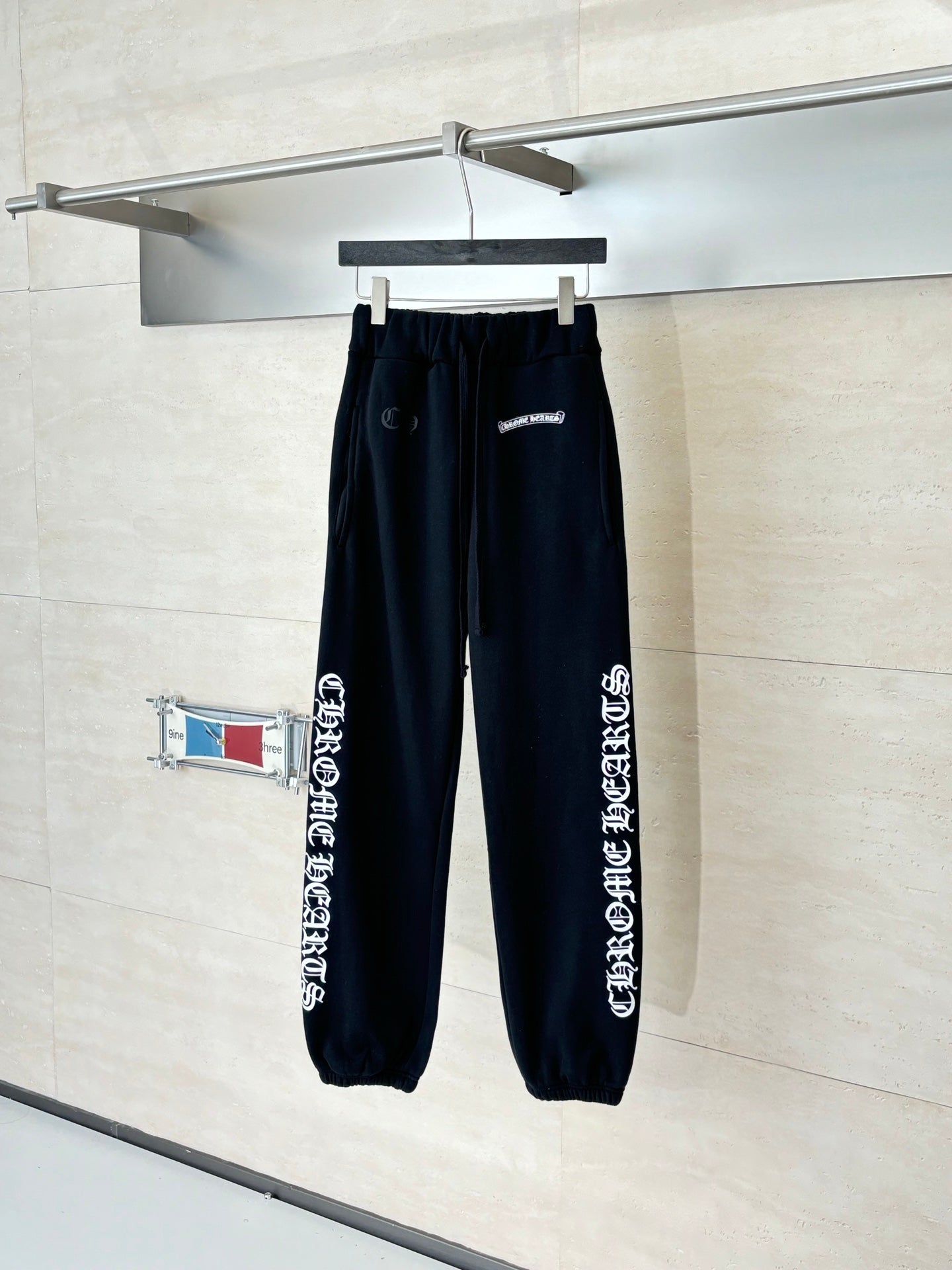 Black jogger pants with elastic cuffs and side graphic print, hanging on a hook