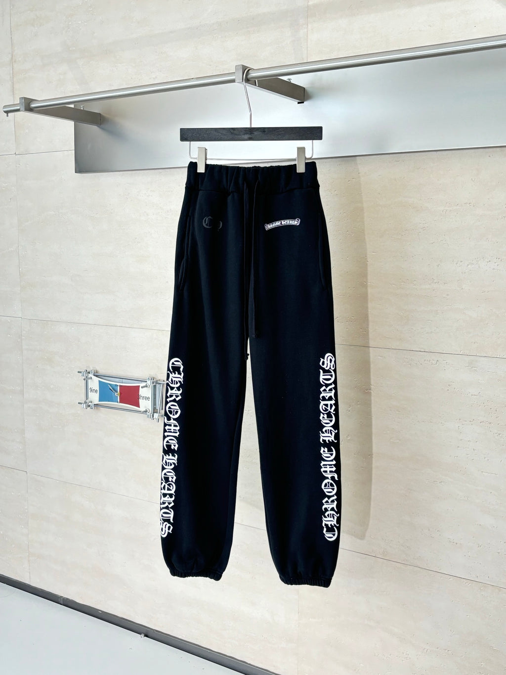 Black sweatpants with side graphic print, elastic waistband and cuffs on a hanger.