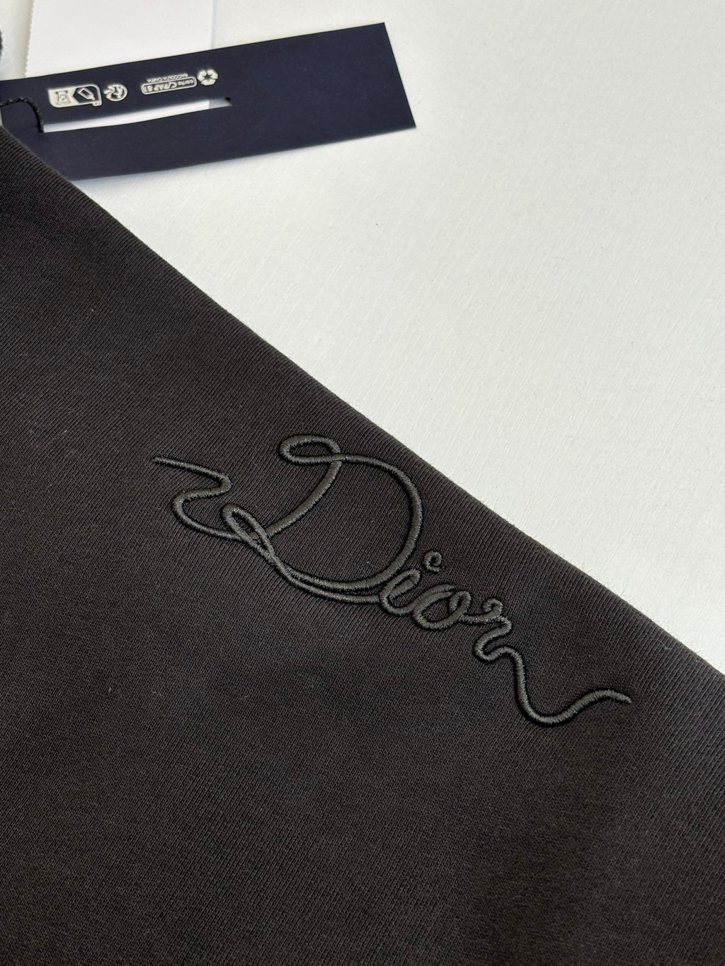 Dark sweatshirt sleeve close-up with embroidered cursive logo