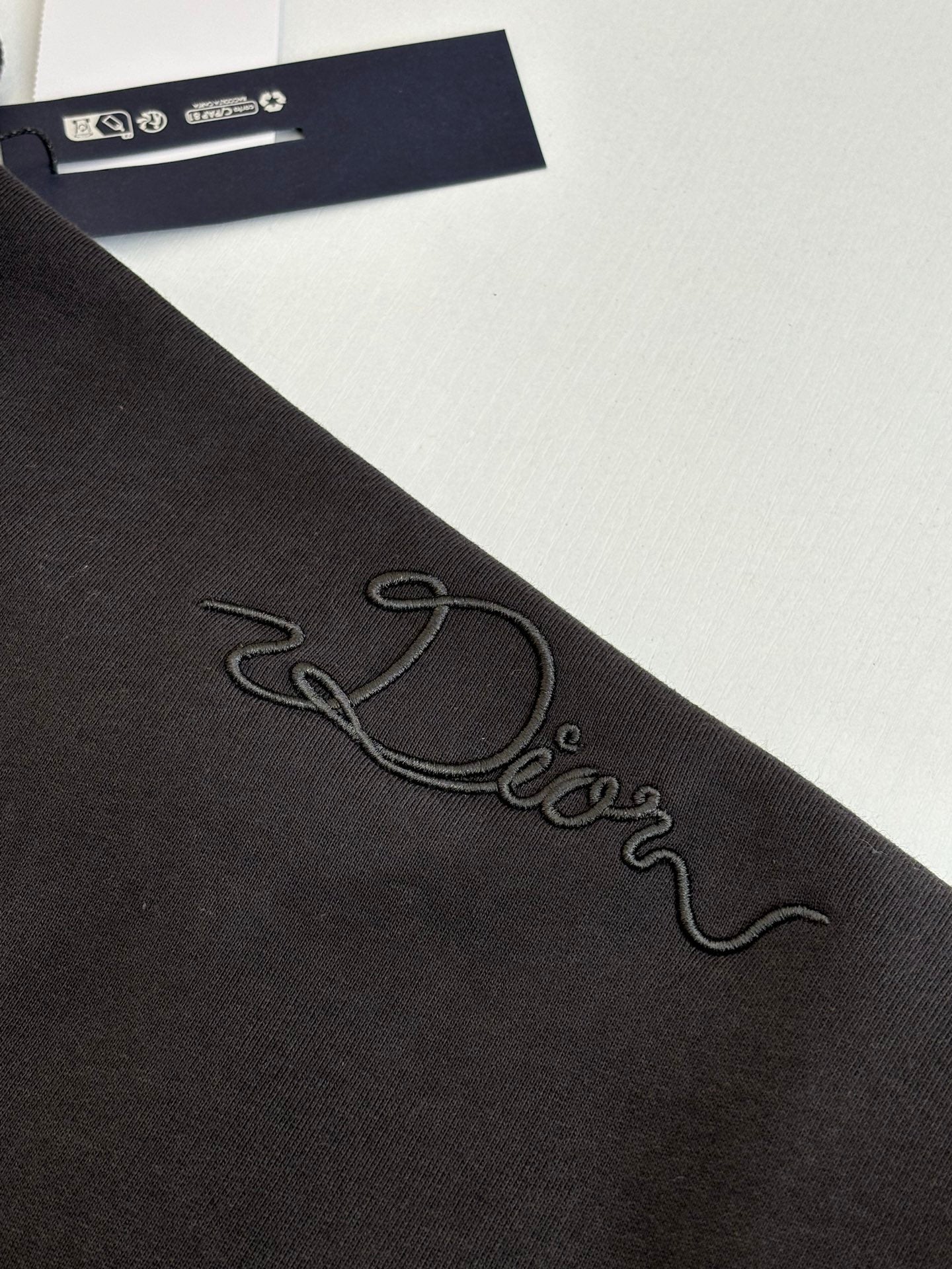 Dark sweatshirt sleeve close-up with embroidered cursive logo