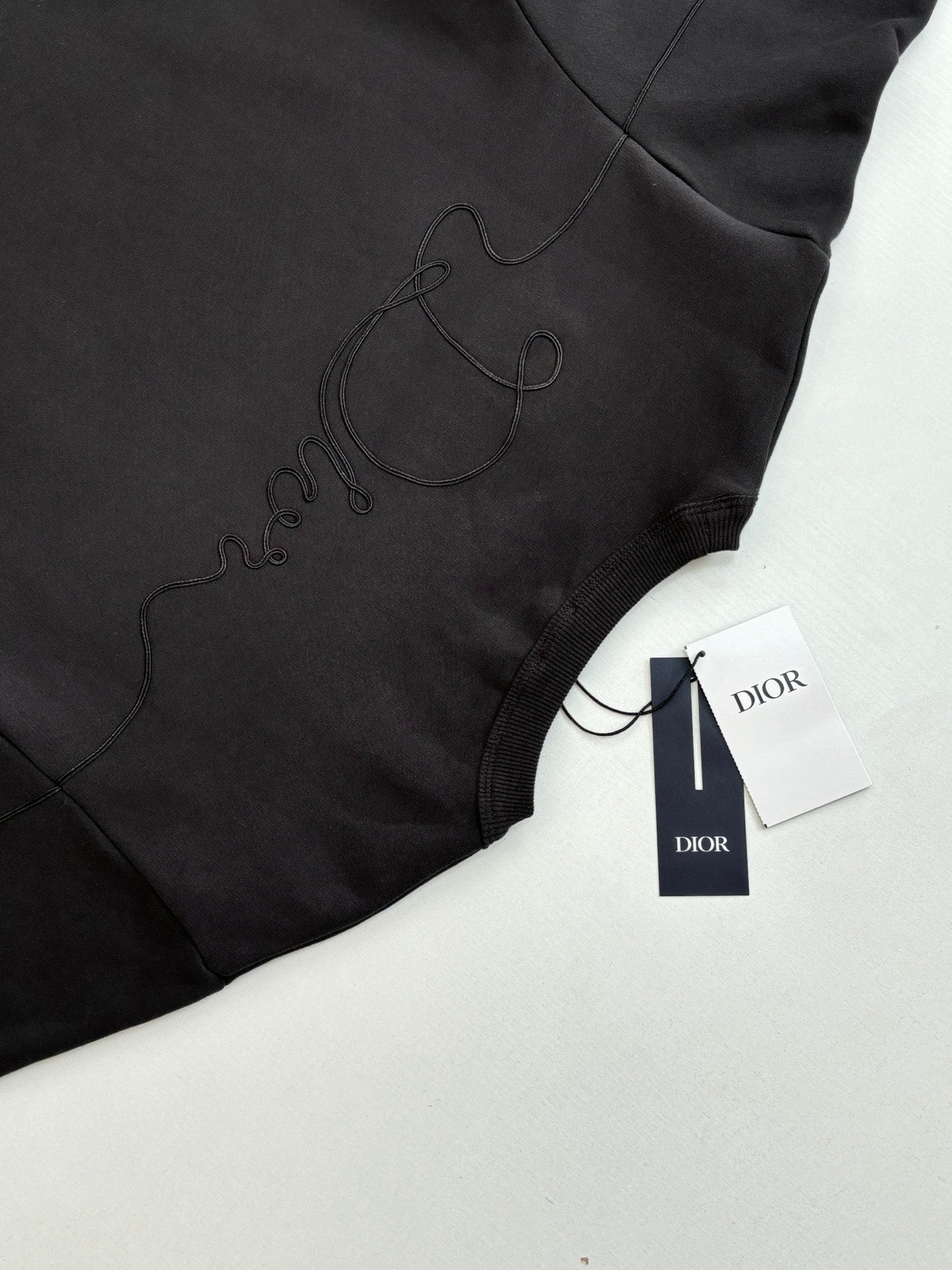 Dark sweatshirt hem close-up with embroidered logo and tag