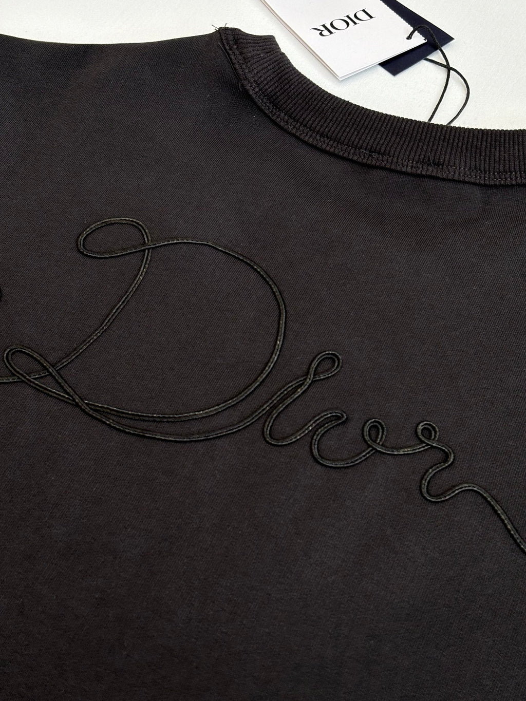 Dark sweatshirt chest close-up with outlined cursive Dior logo embroidery