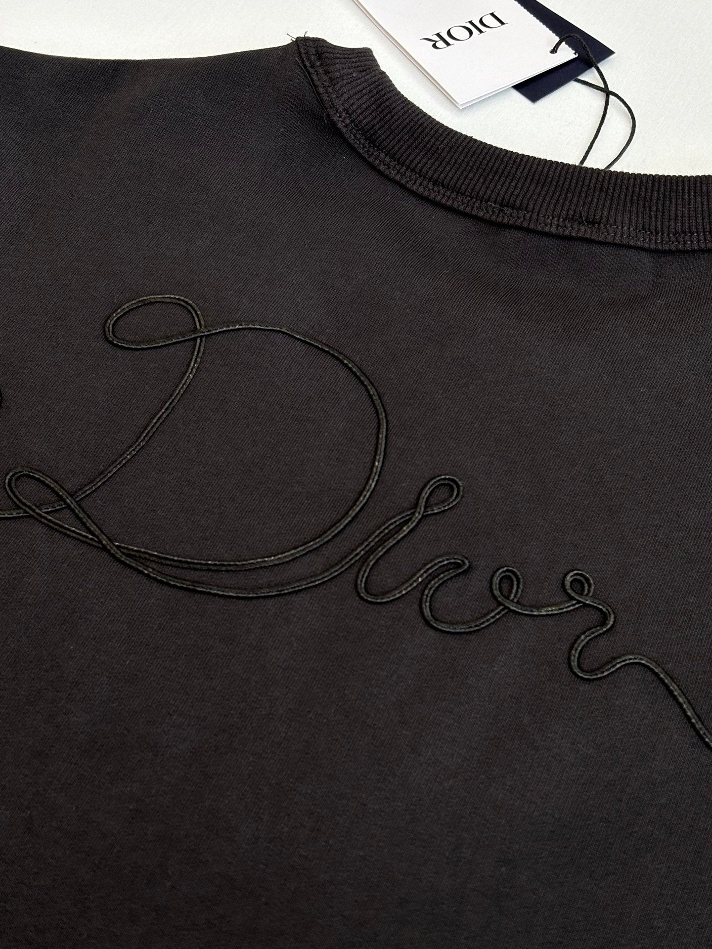 Dark sweatshirt chest close-up with outlined cursive Dior logo embroidery