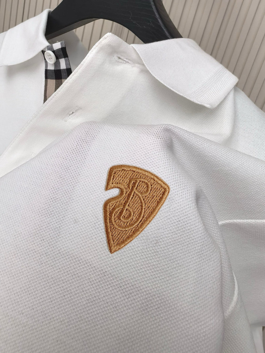White polo shirt close-up with embroidered brown shield-style emblem on chest