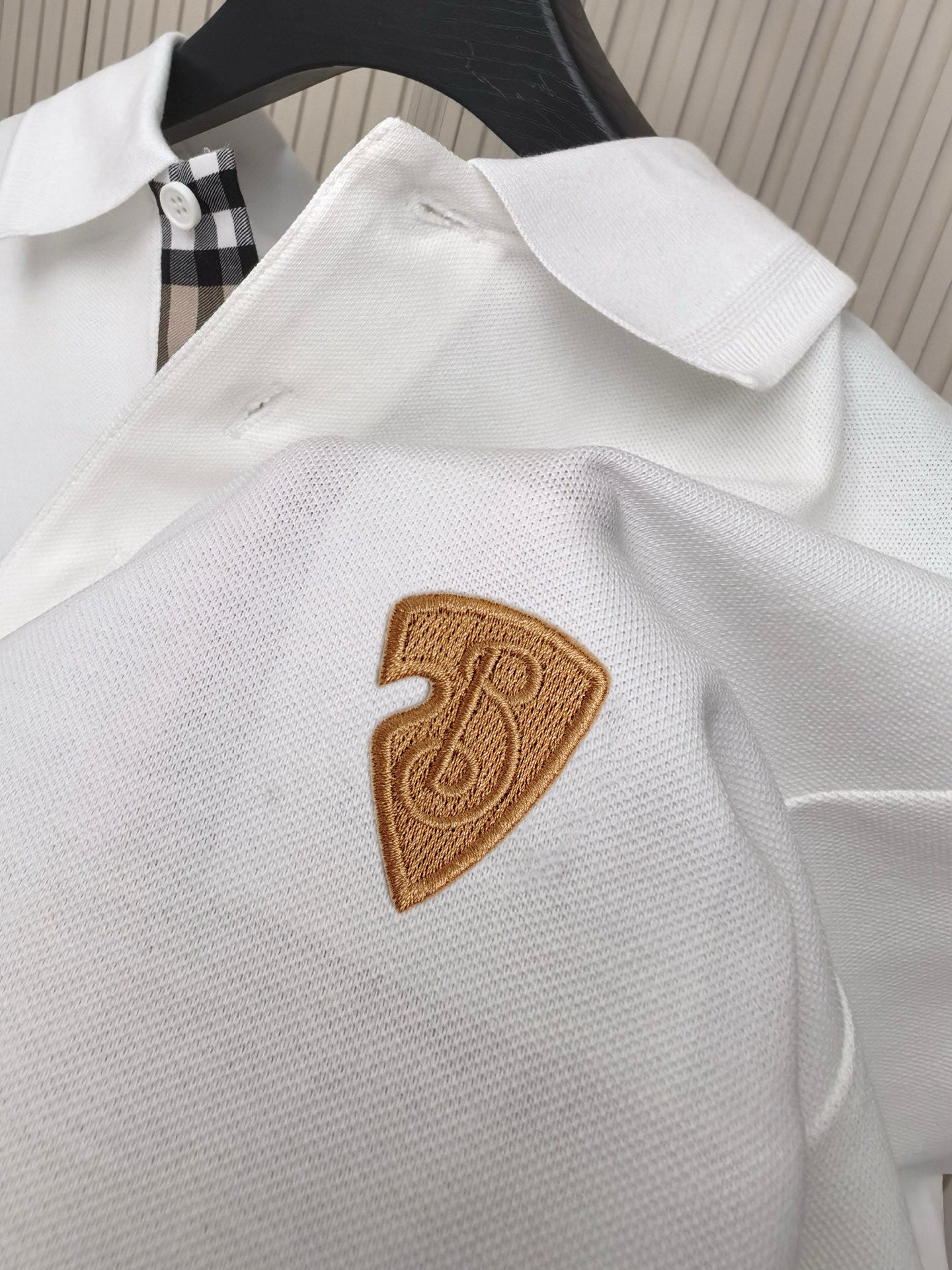 White polo shirt close-up with embroidered brown shield-style emblem on chest