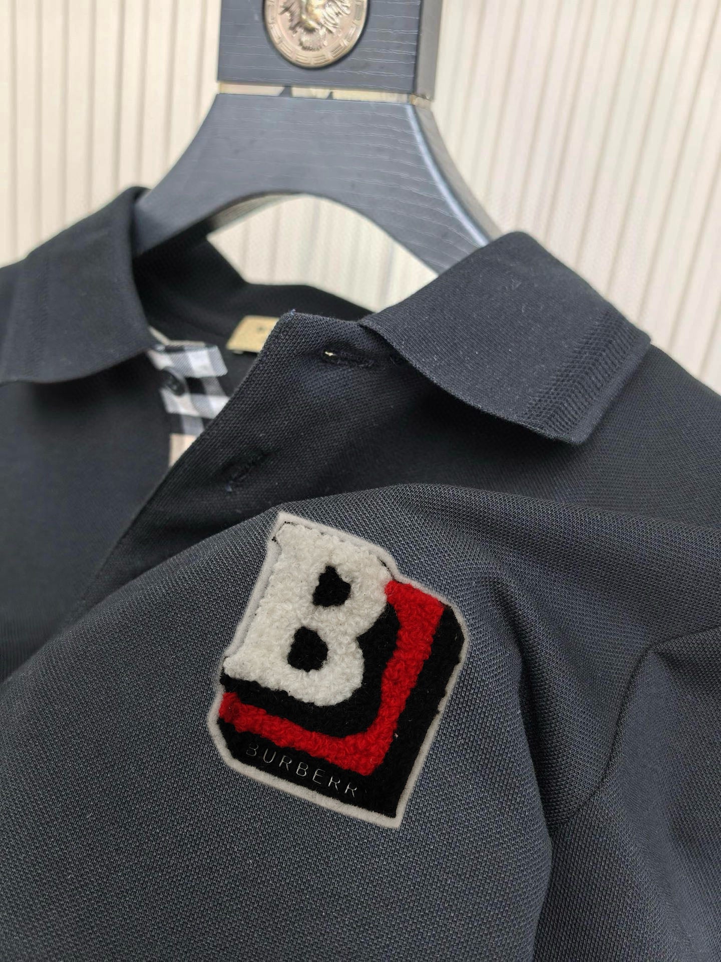 Burberry polo shirt chest patch with B emblem in black, red, and white on dark fabric