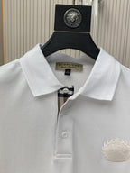 White polo shirt close-up: fold-over collar, button placket, and embroidered chest crest