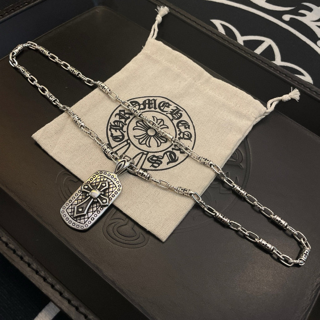 Silver-tone chain necklace with rectangular pendant laid on a dark leather box and pouch.
