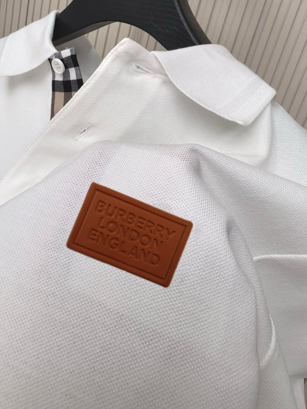 Brown leather-style logo patch on white polo shirt placket