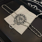 Silver tone chain necklace with round hoop pendant on a light drawstring pouch.