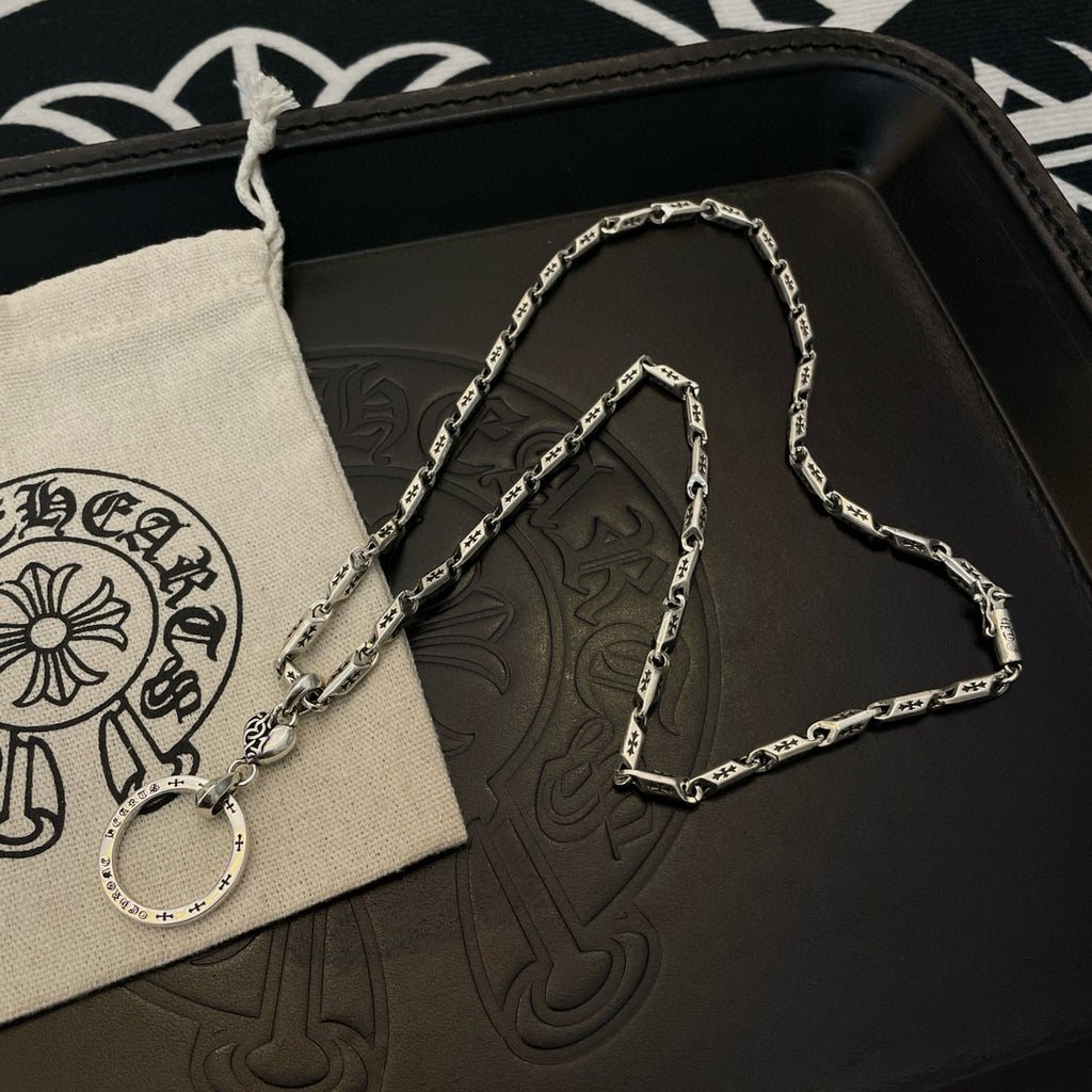 Silver tone chain necklace with round hoop pendant on a black leather pouch.