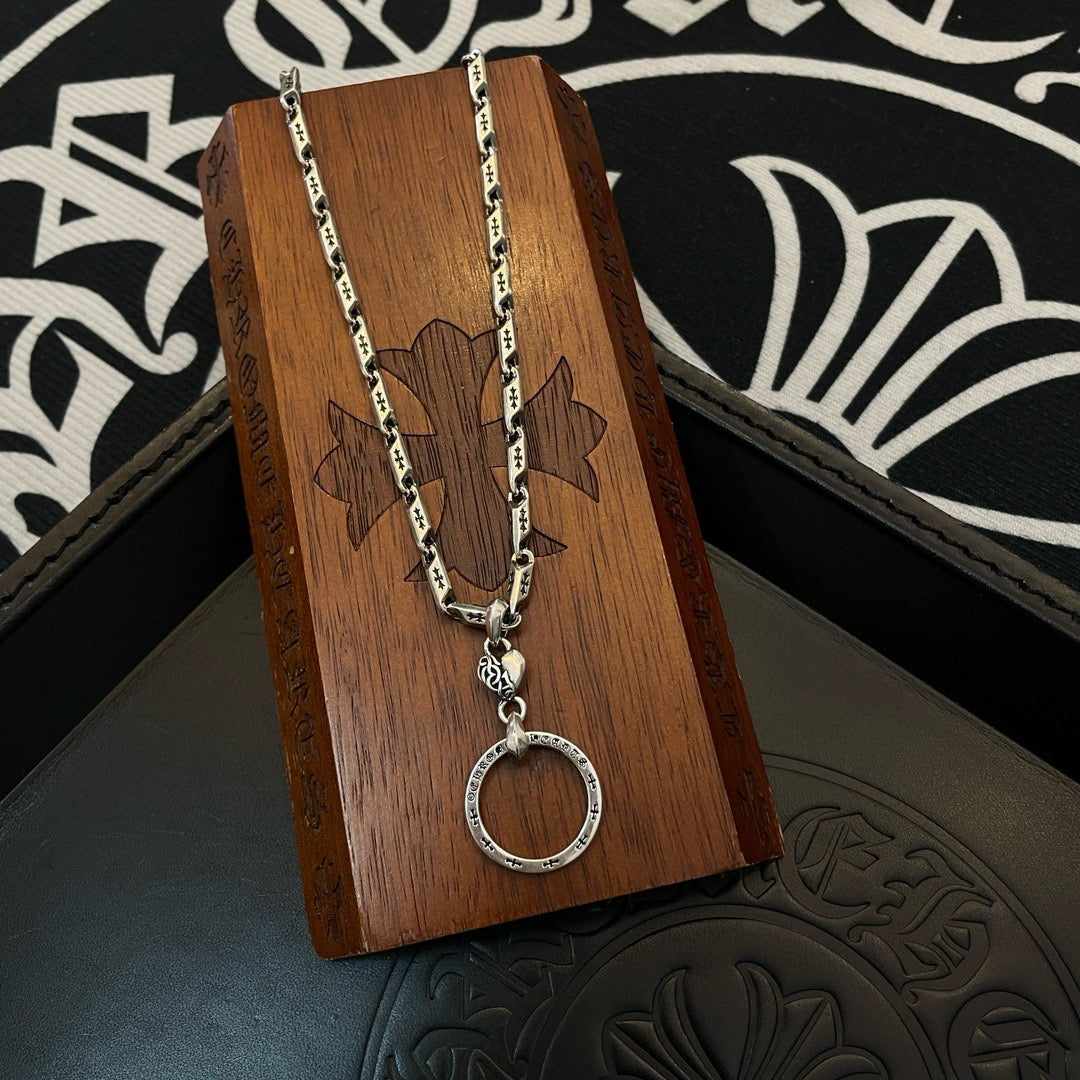 Silver tone chain necklace with round hoop pendant hanging over a wooden display block.